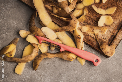 Fresh potato peels with pink peeler on stone background and wooden cutting board, organic kitchen waste concept
