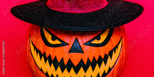 Spooky Halloween jack o' lantern wearing witch hat with scary carved face on vibrant red background for autumn celebration