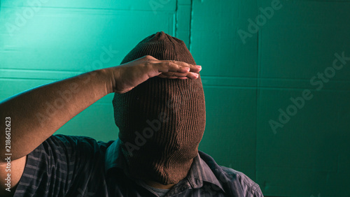 Obraz na płótnie Faceless Indonesian adult male wearing a reversed brown balaclava holding one hand above the covered brow in a searching gesture despite having no vision