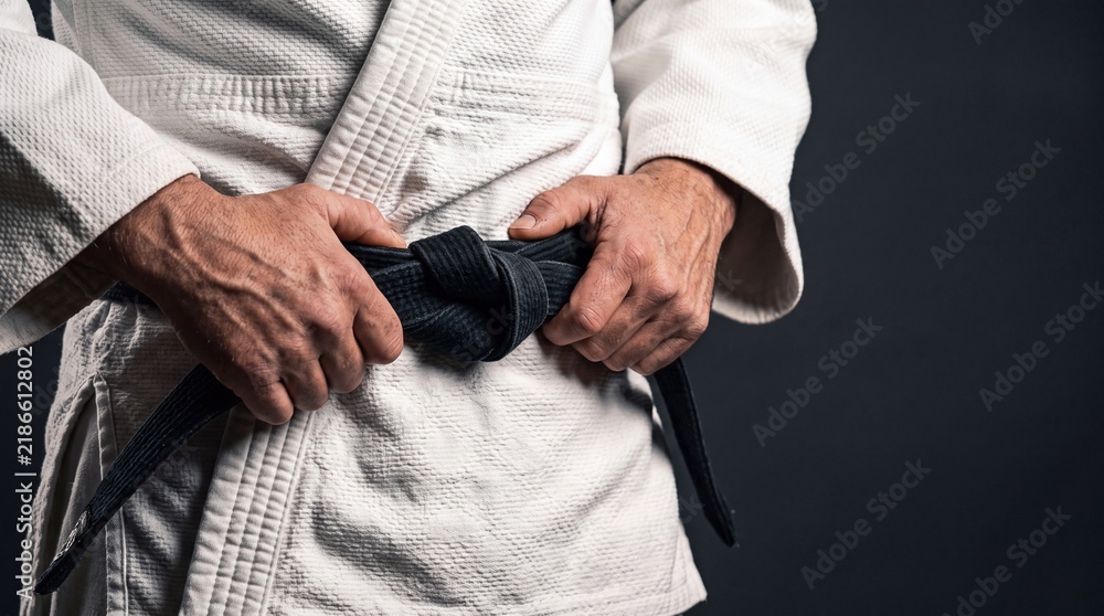 Fototapeta premium Close up of a martial artist's hands tying a black belt around their traditional uniform against a dark background