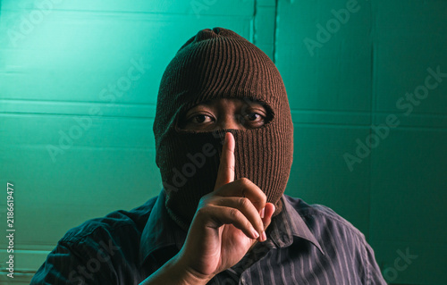 Foto Secretive Indonesian adult male wearing brown balaclava mask making silence gest