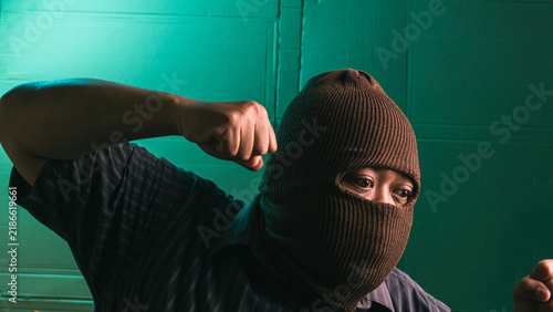 Fotografie Aggressive Indonesian adult male wearing brown balaclava mask raising clenched f
