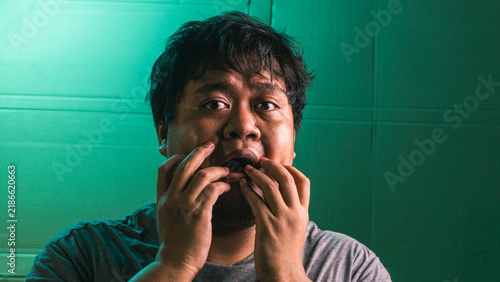 Fotografie An astonished young indonesian male touches the mouth area with the fingers, displaying a wide open jaw and immense disbelief against a green textured background