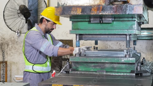 Industrial worker wearing safety helmet and reflective vest operating metal forming machine and industrial press inside factory, focused metal fabrication task beside heavy machinery and protective
