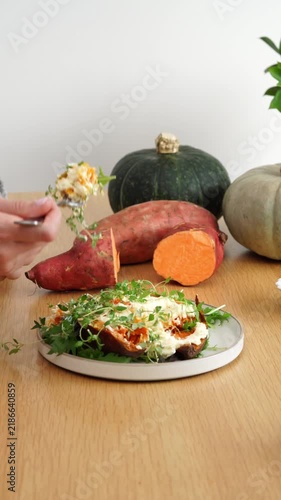 Closeup hand takes a sweet potato and feta from the plate on rustic homemade wooden kitchen table during autumn