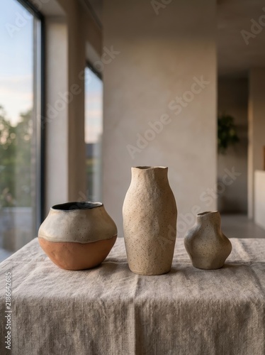 Three uniquely shaped ceramic vases handcrafted with textured surfaces, displayed on a linen tablecloth in a modern, naturally lit interior