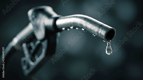 Macro close-up of a metal gas pump nozzle with a single dripping gasoline drop against a dark blurred background