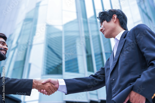 Canvas Print Two male executives grip hands in a decisive business handshake along a sunlit w