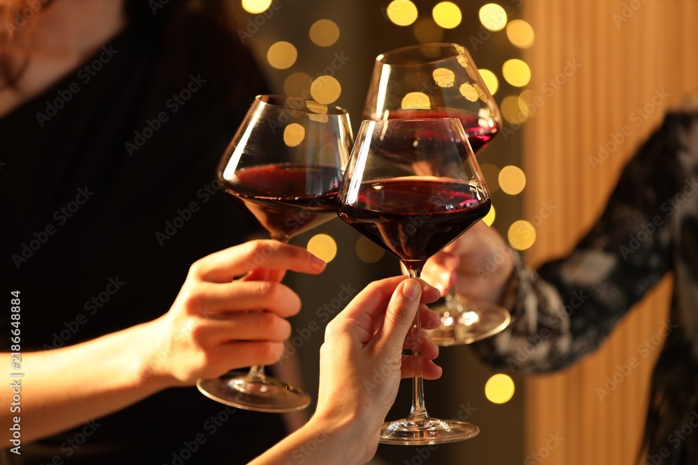 Obraz premium Friends clinking glasses of wine against blurred lights indoors, closeup
