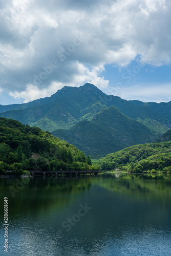 Obraz na płótnie Towering green mountain peaks reflect upon the calm waters of a scenic lake beneath dramatic cloudy skies in South Korea