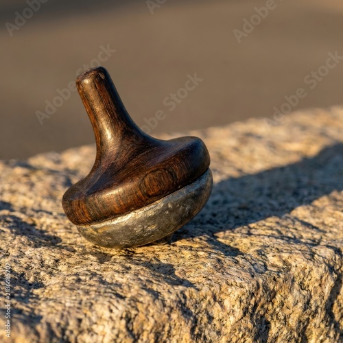 Handcrafted Wood and Metal Spinning Top Resting on Granite Ledge Outdoors