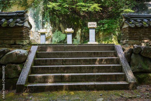 Foto Ancient stone stairs flanked by tiled earthen walls lead to sacred memorial steles at a Korean temple stupa field