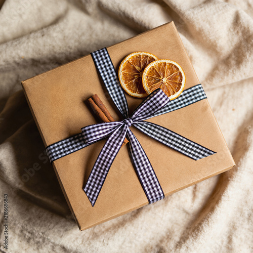 Kraft gift box with gingham ribbon, dried orange slices and cinnamon sticks on cream fabric