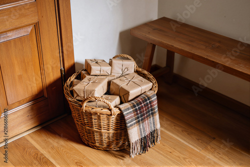 Wicker basket filled with kraft paper gifts and a plaid blanket by a wooden door