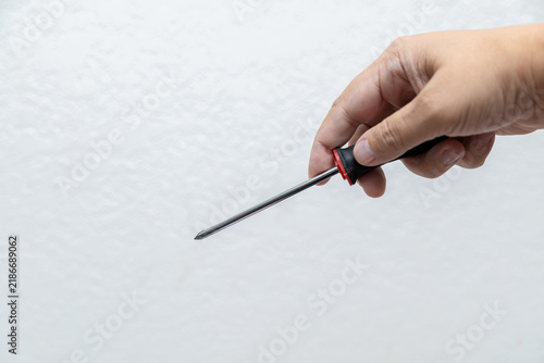 Obraz na plátně Hand holding Phillips screwdriver with black and red handle against light neutra