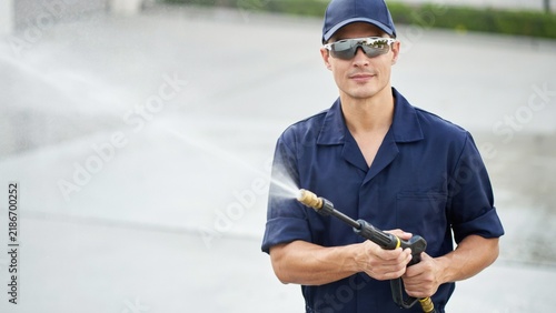 Professional pressure washer wearing a blue uniform and mirrored sunglasses, holding a pressure washing wand in a misty spray.