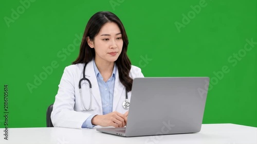 Female doctor participating in an online medical consultation using a laptop against a clean green screen background for remote healthcare communication concepts.