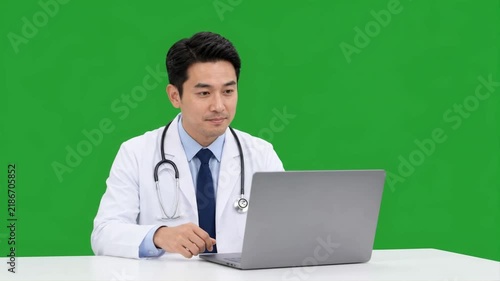 Male doctor participating in an online medical consultation using a laptop against a clean green screen background for remote healthcare communication concepts.