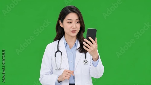 Female doctor providing a telemedicine consultation using a smartphone against a clean green screen background for digital healthcare and remote medical concepts.