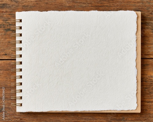 Blank spiral notebook with textured deckle edge paper resting on a rustic wooden background