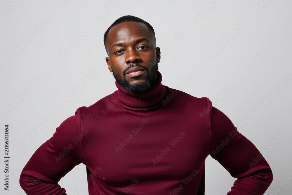 Obraz premium Confident man in maroon turtleneck posing with hands on hips against white wall