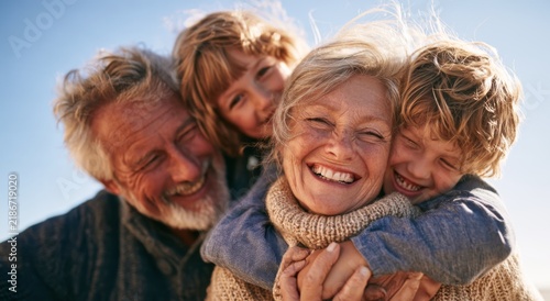 Happy grandparents and grandchildren embracing outdoors under clear blue sky