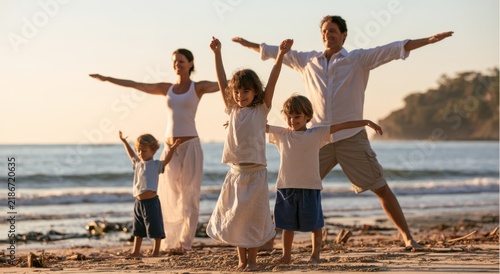 Happy family with two children standing on the beach with arms outstretched