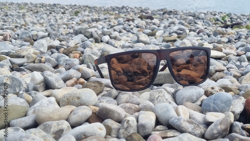 Sunglasses resting on a rocky shore. The lenses reflect the surrounding stones, creating an interesting pattern