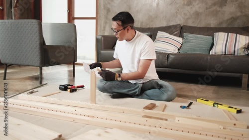 Asian mature man self-assembling flat-pack furniture with DIY tools and instruction guide, confused with wooden parts, home improvement, craft installation, hobby workshop, handyman active lifestyle.