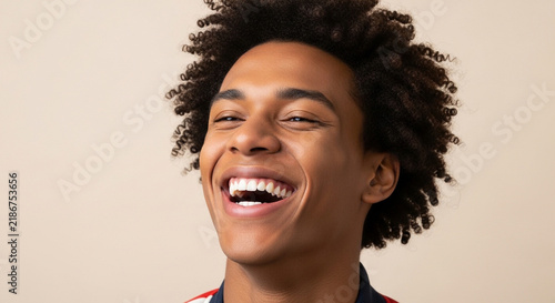 Young man with curly hair laughing against a neutral studio background