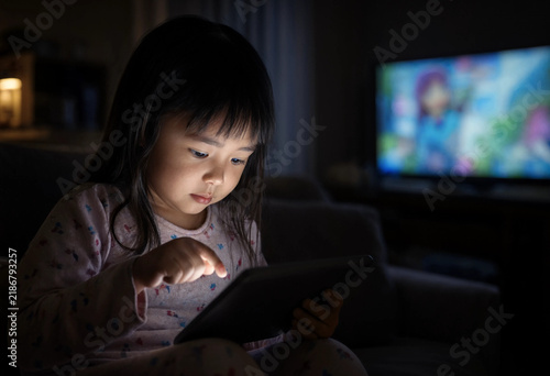 Little girl focused on tablet in dimly lit room