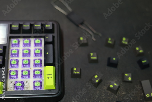 A top-down view of a mechanical numpad assembly displaying purple hot-swap switches. Black keycaps with distinct lime green legends and accents are scattered nearby, alongside a standar