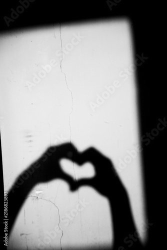 Close up black and white shadow of heart shape hand gesture on the dirty wall