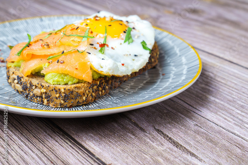 Bild auf Leinwand Healthy avocado toast topped with smoked salmon, fried egg and mixed seeds on mu