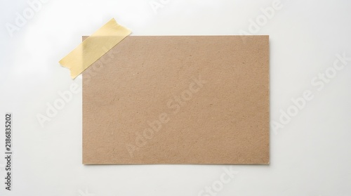 Blank brown kraft paper sheet pinned on white wall with yellow masking tape for creative or packaging design background