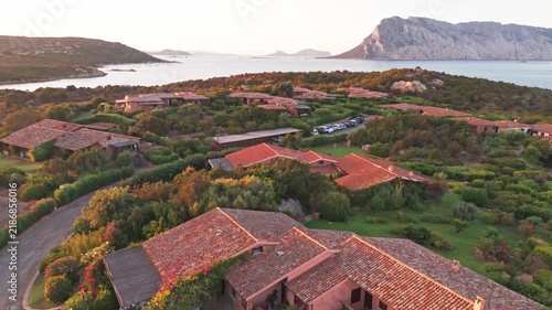 Beautiful aerial view of a luxury resort with terracotta roofs nestled in the lush green landscape of sardinia, overlooking the sea at sunset