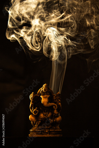 Ganesha statue with swirling incense smoke on a dark background for spiritual meditation.