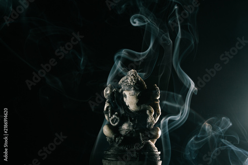 Ganesha statue with swirling incense smoke on a dark background for spiritual concepts.