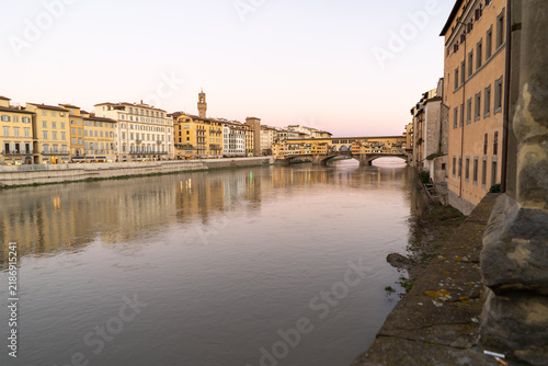 The iconic Ponte Vecchio bridge spans the Arno River in Florence, Italy, reflecting the historic buildings along its banks during twilight