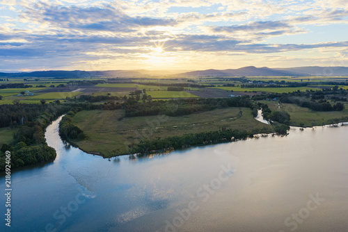 Aerial view of sunset over sugar cane fields and farmland on Palmers Island near Yamba, with warm golden light illuminating the cultivated rural landscape beneath a dramatic evening sky 