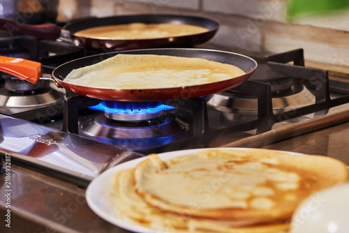 Cooking at home in the kitchen according to recipe from the Internet. Pancakes are fried in pans on a gas oven. Step by step recipe.