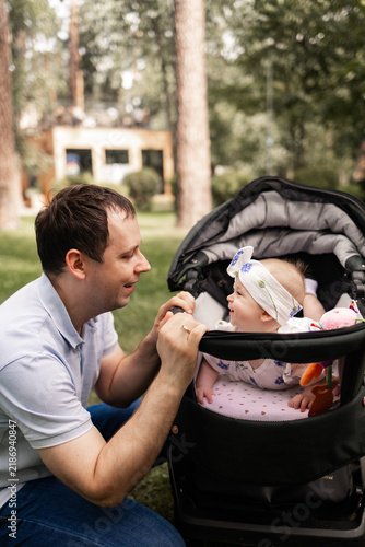 Obraz na płótnie Close family moment as a father gently holds his toddler’s hand while the child sits safely in a stroller during a summer walk with parents in a green park