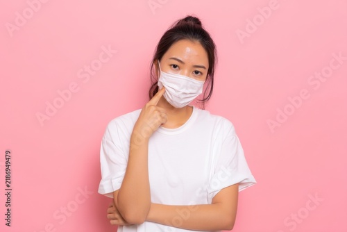 Young woman wearing a protective mask making thoughtful gestures against a pink background with a casual outfit expressing health awareness and personal care. Generative AI
