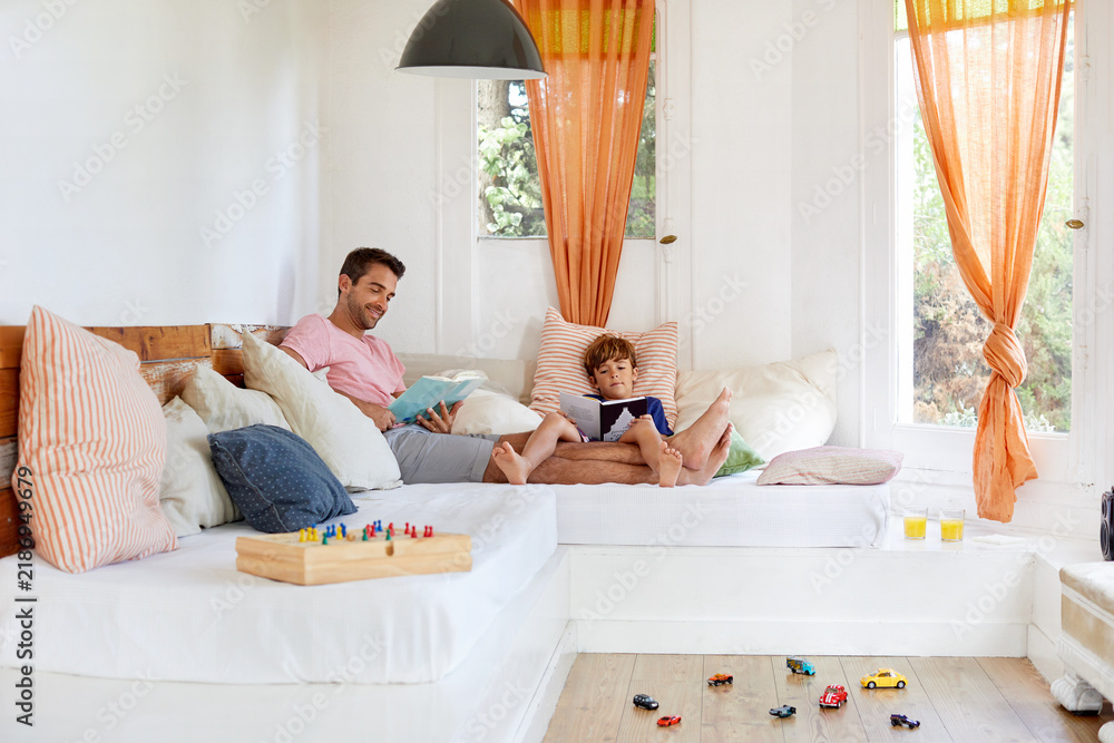 Fototapeta premium Love, book and reading with father and son on sofa in home for connection, relax and storytelling. Education, knowledge and support with man and child in living room in family house for fairytale
