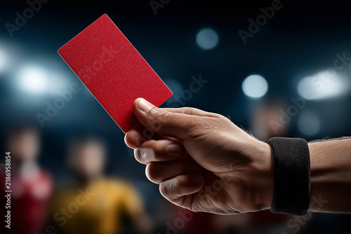 Soccer referee holding a red card in the air during a match, representing foul play, penalty, misconduct, disciplinary action and controversial moments in football