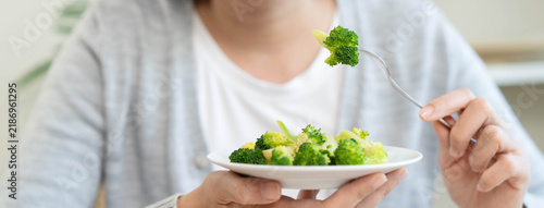 Fotografie Close up of a woman hand holding fork with green broccoli over a white plate for