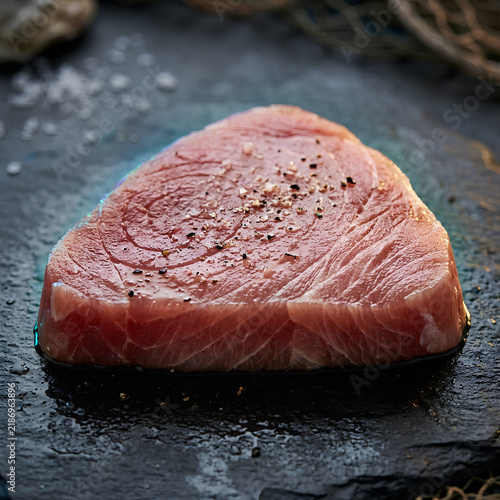 Raw Beef Steak on Dark Surface with Salt and Pepper.