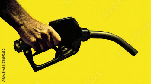 illustration of human hand holding black fuel dispenser nozzle with visible hose curve, isolated on bright yellow primary background. High contrast lighting enhances texture and contours while 