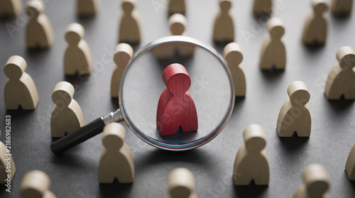 Wooden figures representing people with one distinct red leader under a magnifying glass.