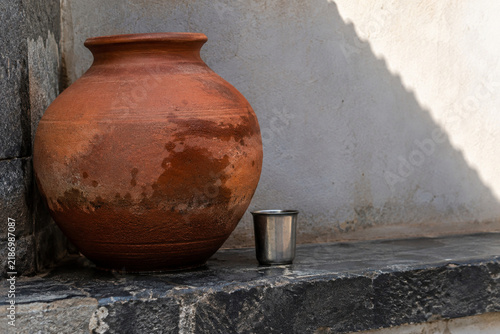 фотографія Damp Terracotta Water Jar with a Metal Cup on a Shaded Ledge